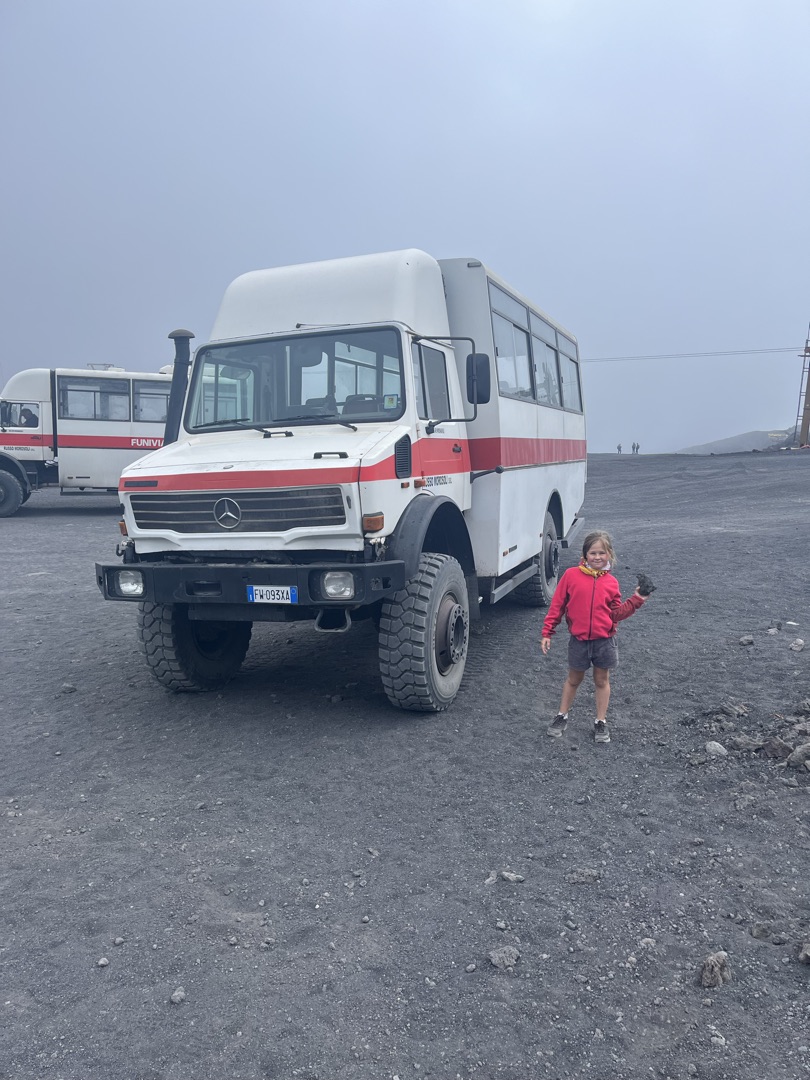 Agathe en veste violette courant près d'un grand champ vert sous un ciel gris.